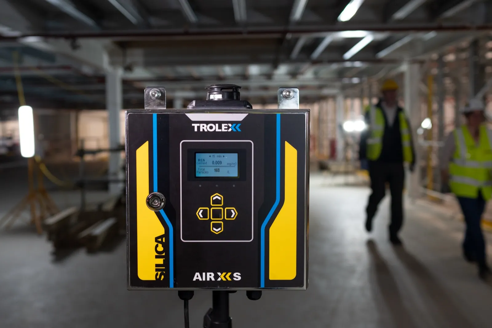 Monitor de sílice cristalina TROLEX AIR XS instalado en una planta industrial con trabajadores al fondo